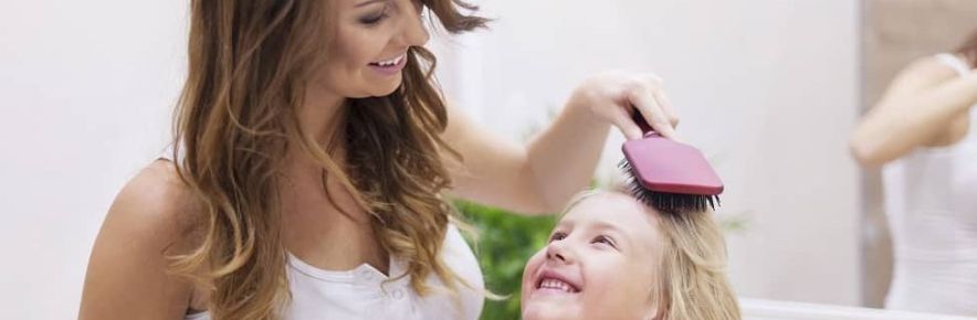 mère qui coiffe les cheveux de sa fille avec une brosse rose