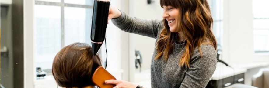 professionnelle de la coiffure qui sèche les cheveux d'une cliente